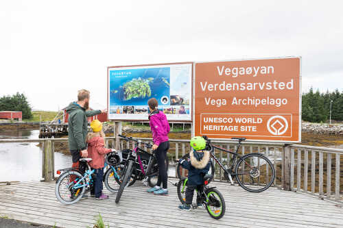 Bilde av familie på sykkel som står å ser på skilt på Vega.