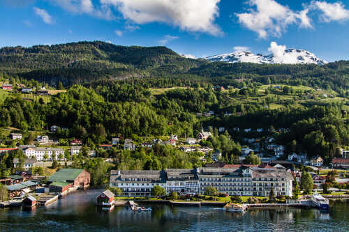 Bilde av Ulvik med bygninger, hotell og fjell med blå himmel.