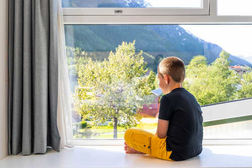 Bilde av gutt som sitter i vinduskarm på Fru Haugans og ser ut.