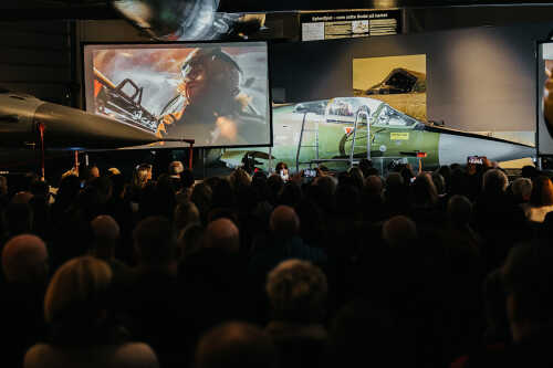 Bilde fra konferanse med Ann-Jorid på skjem som jagerflypilot, publikum i salen.