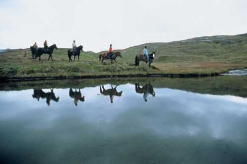 Bilde av ryttere på tur i ved vann i norsk natur.